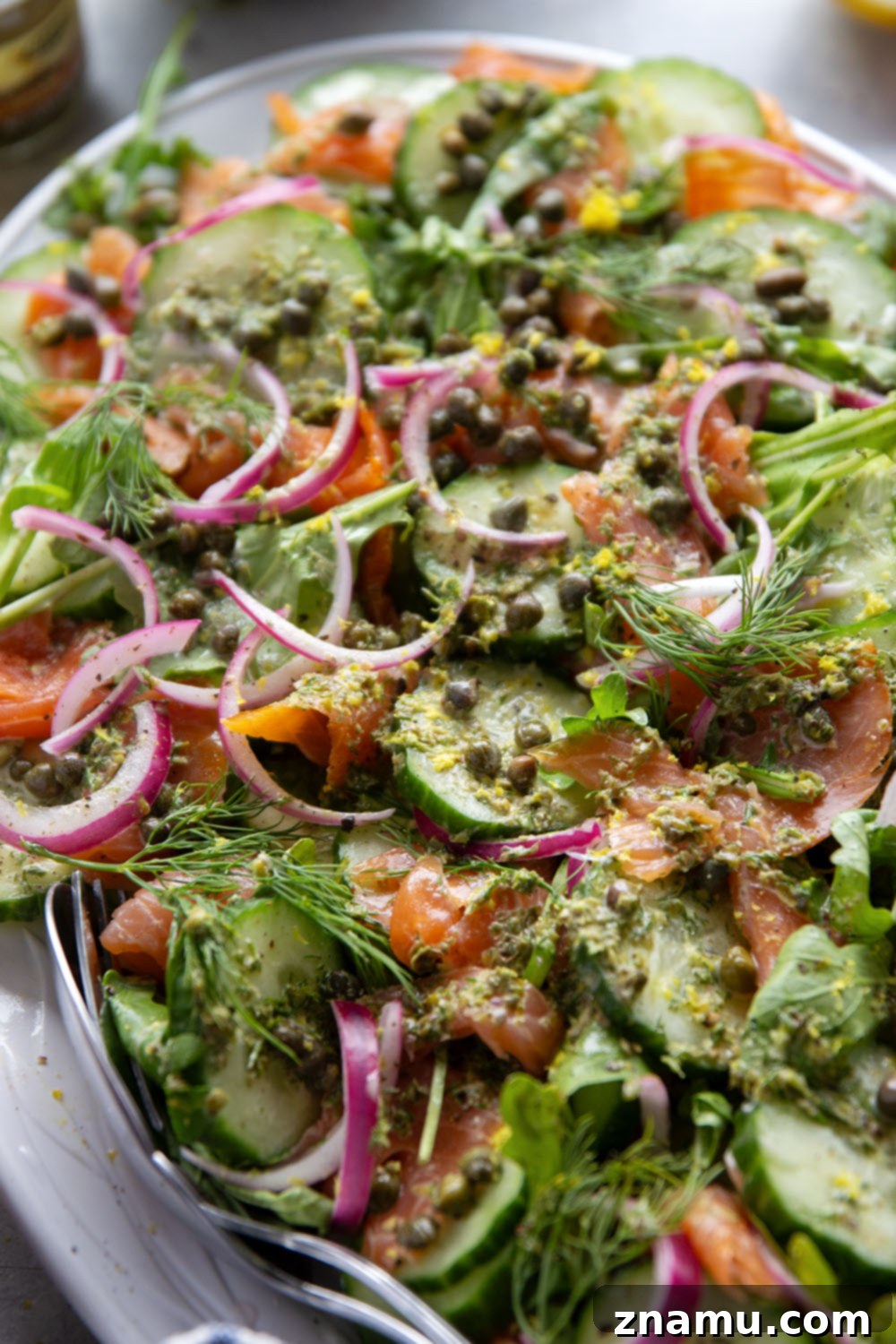 Close-up shot of Smoked Salmon Cucumber Salad with creamy dill dressing being drizzled over the top.