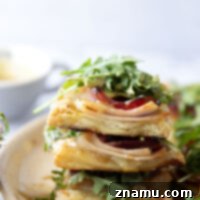 These savory cordon bleu puff pastry tarts have everything you'll find in the classic chicken dish in hand-held tart form! These tarts feature layers of deli ham, chicken, and Swiss cheese slices with a tangy honey mustard and lots of arugula piled on top.