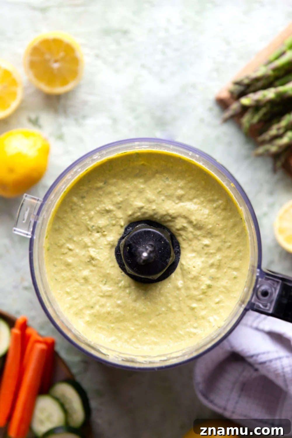 Emerald Asparagus Pea Hummus 4 A bowl of freshly made asparagus pea hummus, beautifully garnished with a drizzle of olive oil, a sprig of fresh parsley, and a few whole peas.